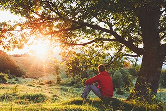 man sat watching sunset alone in a field