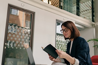 Woman reading book in front of laptop
