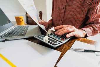 man typing on calculator with laptop on desk