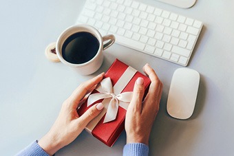 Person holding a red present box next to a computer keyboard