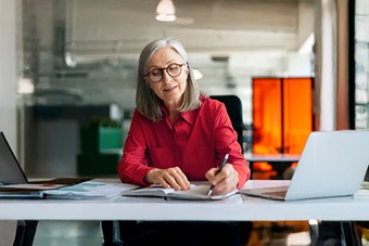 Woman in a red shirt at a desk writing in her notebook