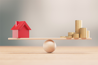 Toy house and coins balancing on a scale 