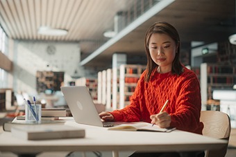 Woman on desk with laptop, writing