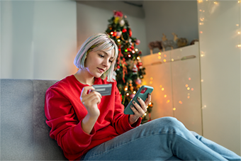 woman holding credit card and phone by Christmas tree