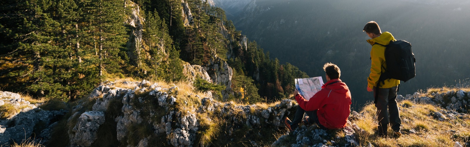 Two men reading a map sat on top of a mountain