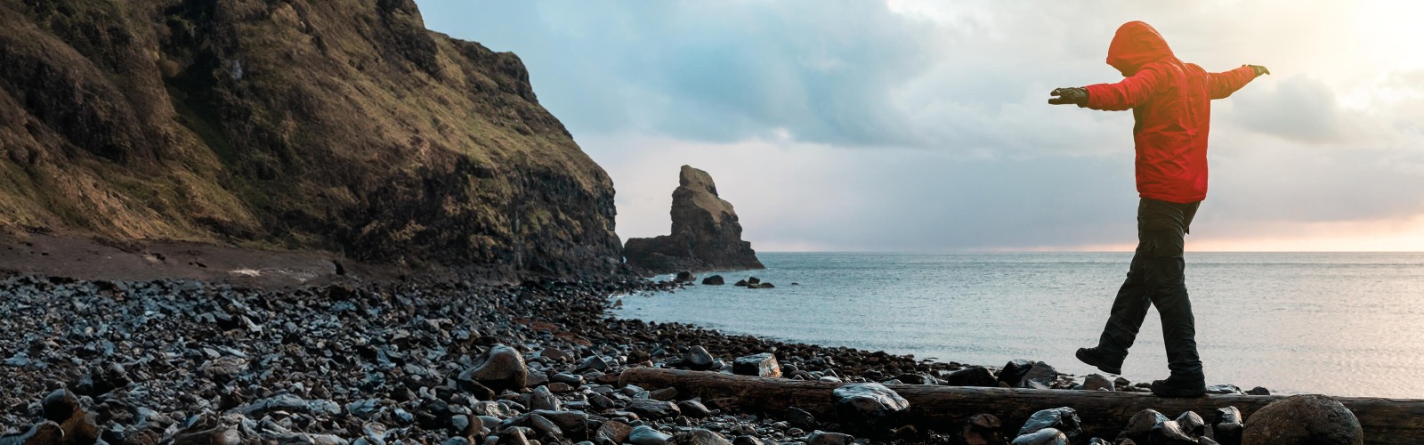 Person in red coat walking along rocky beach