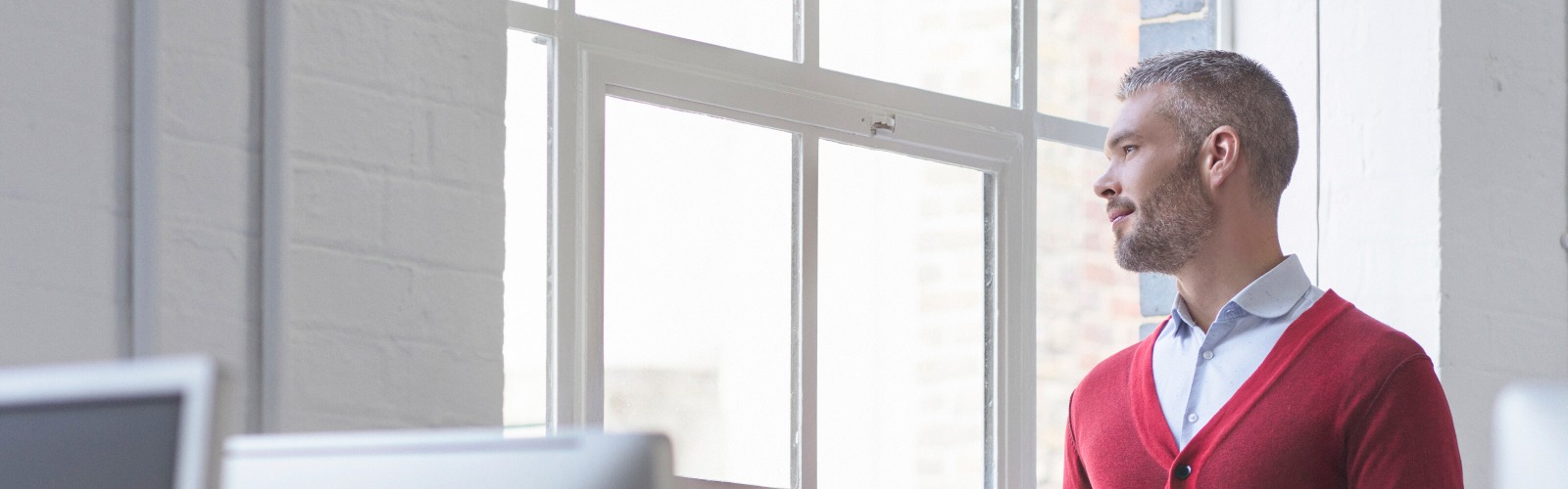 Man in red cardigan looking out of window 