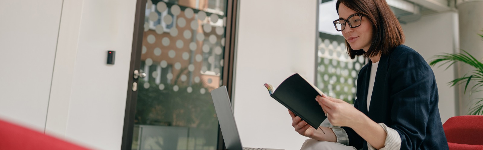 Woman reading book in front of laptop