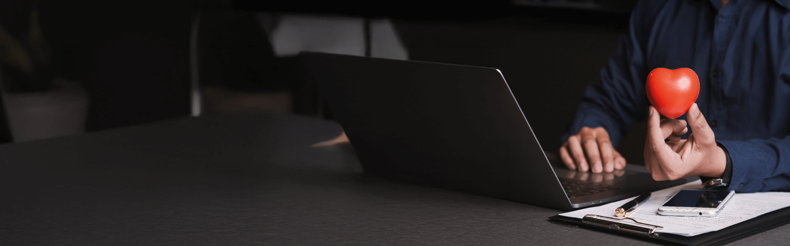 man typing on laptop holding a heart shaped balloon