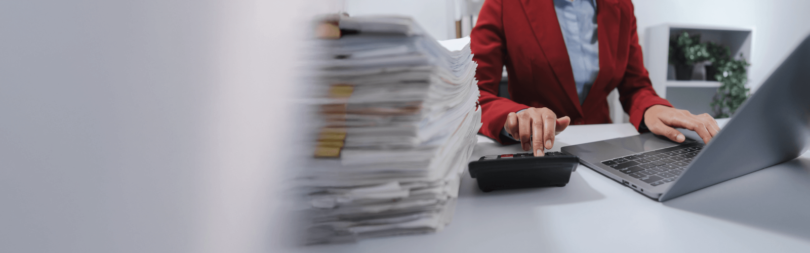 woman typing on calculator next to stack of papers