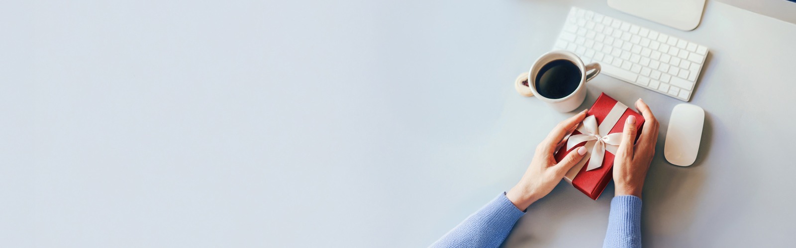 Person holding a red present box next to a computer keyboard