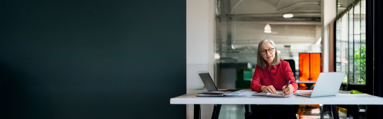 Woman in a red shirt at a desk writing in her notebook