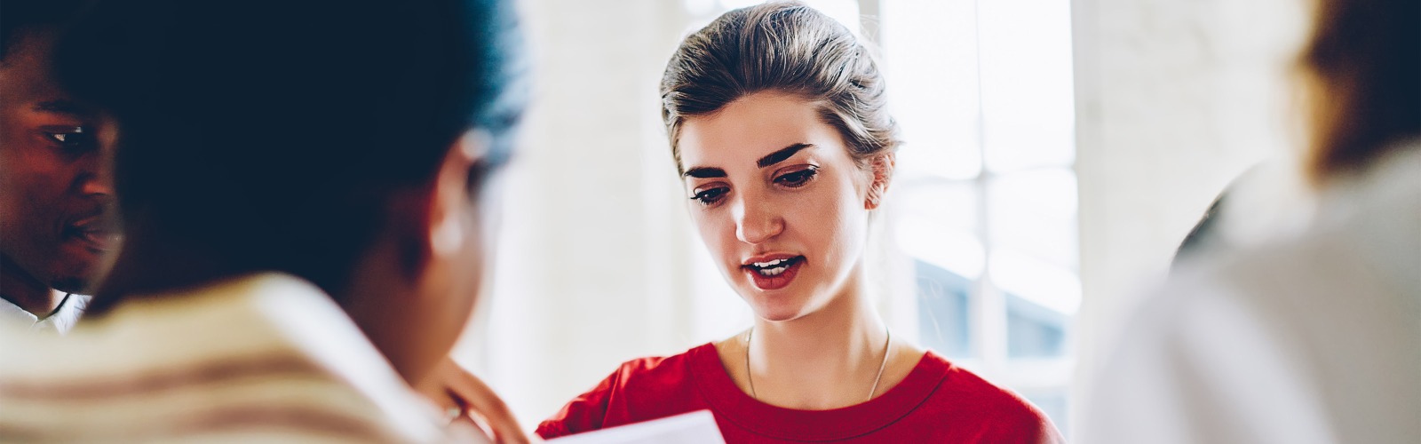 woman with a red jumper on reading in a meeting with two other people