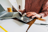 man typing on calculator with laptop on desk